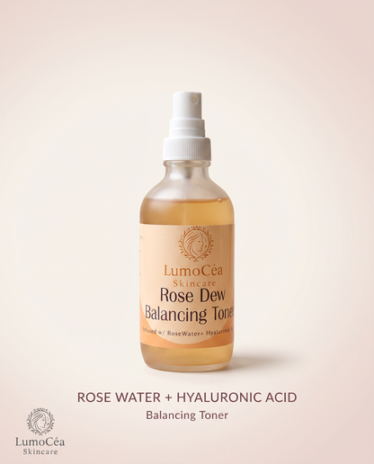 A bottle of LumiCea Skincare Rose Dew Balancing Toner, featuring a clear glass bottle filled with a golden-amber liquid, a white spray nozzle, and a beige label. The product is centered on a soft beige background with descriptive text below.